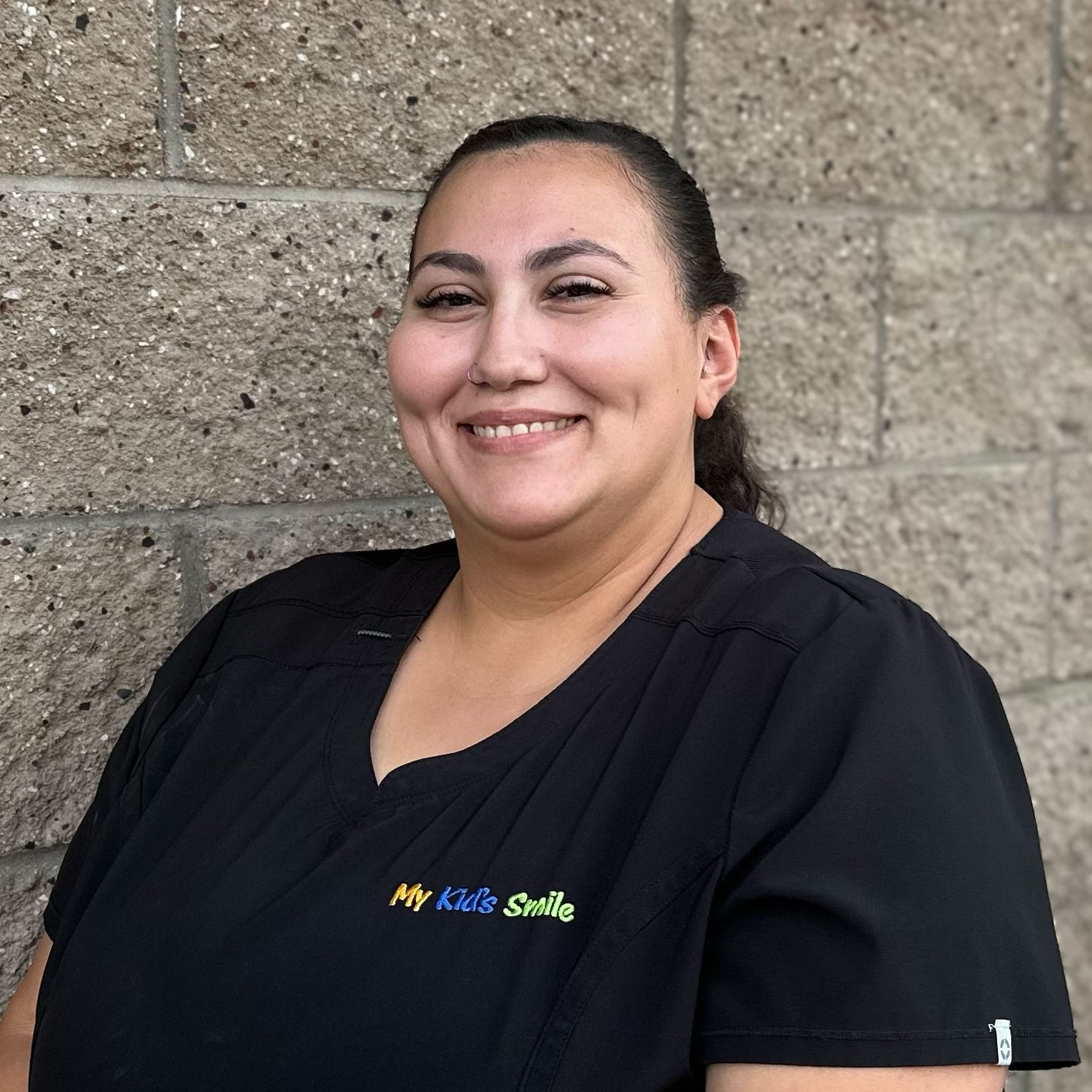 Person smiling in black uniform, brick wall background.