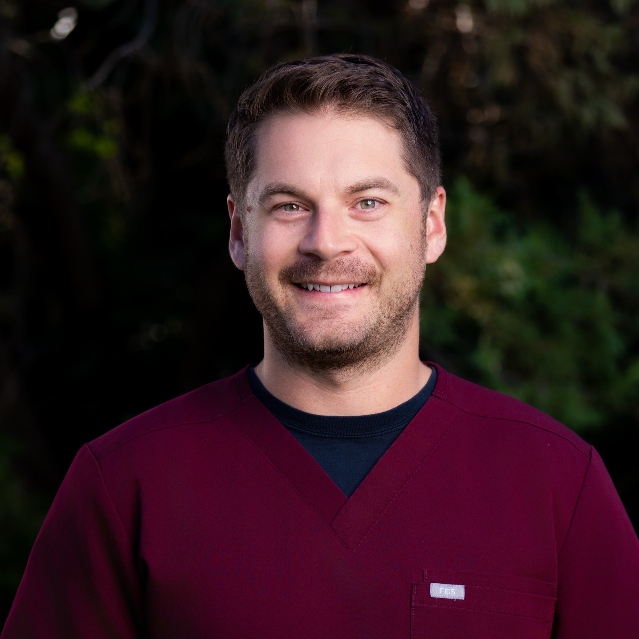 Smiling man in maroon medical uniform.